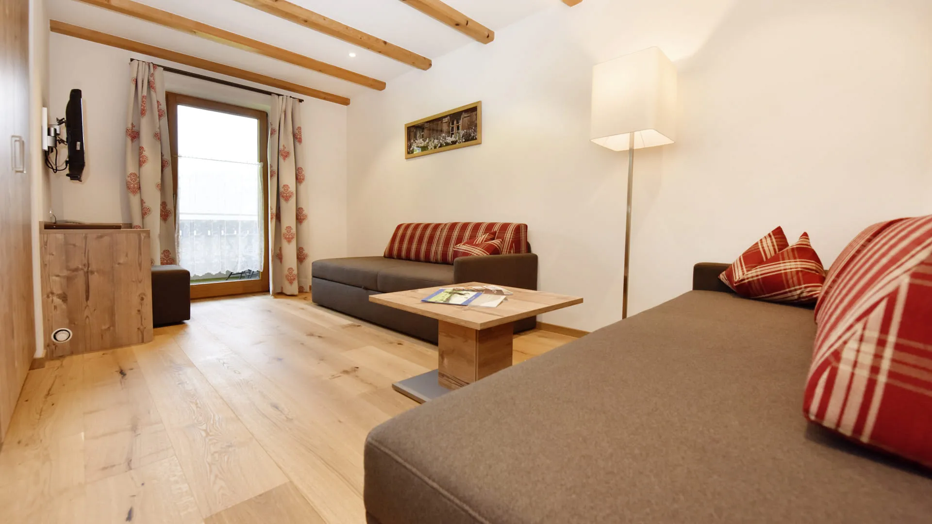 Heller Wohnraum mit Holzdecke, Sofa und Fenster mit Vorhängen.