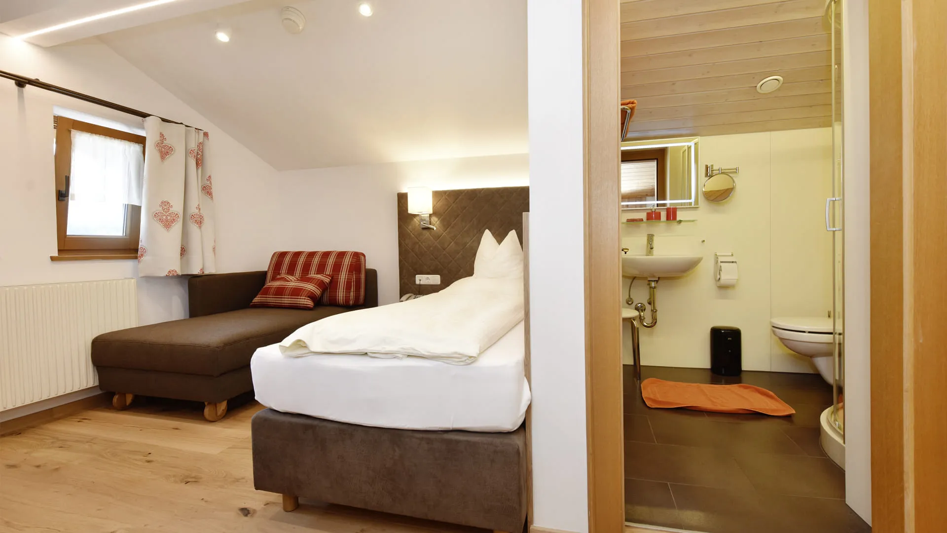 Helles Zimmer mit Bett, Sofa und angrenzendem Badezimmer.