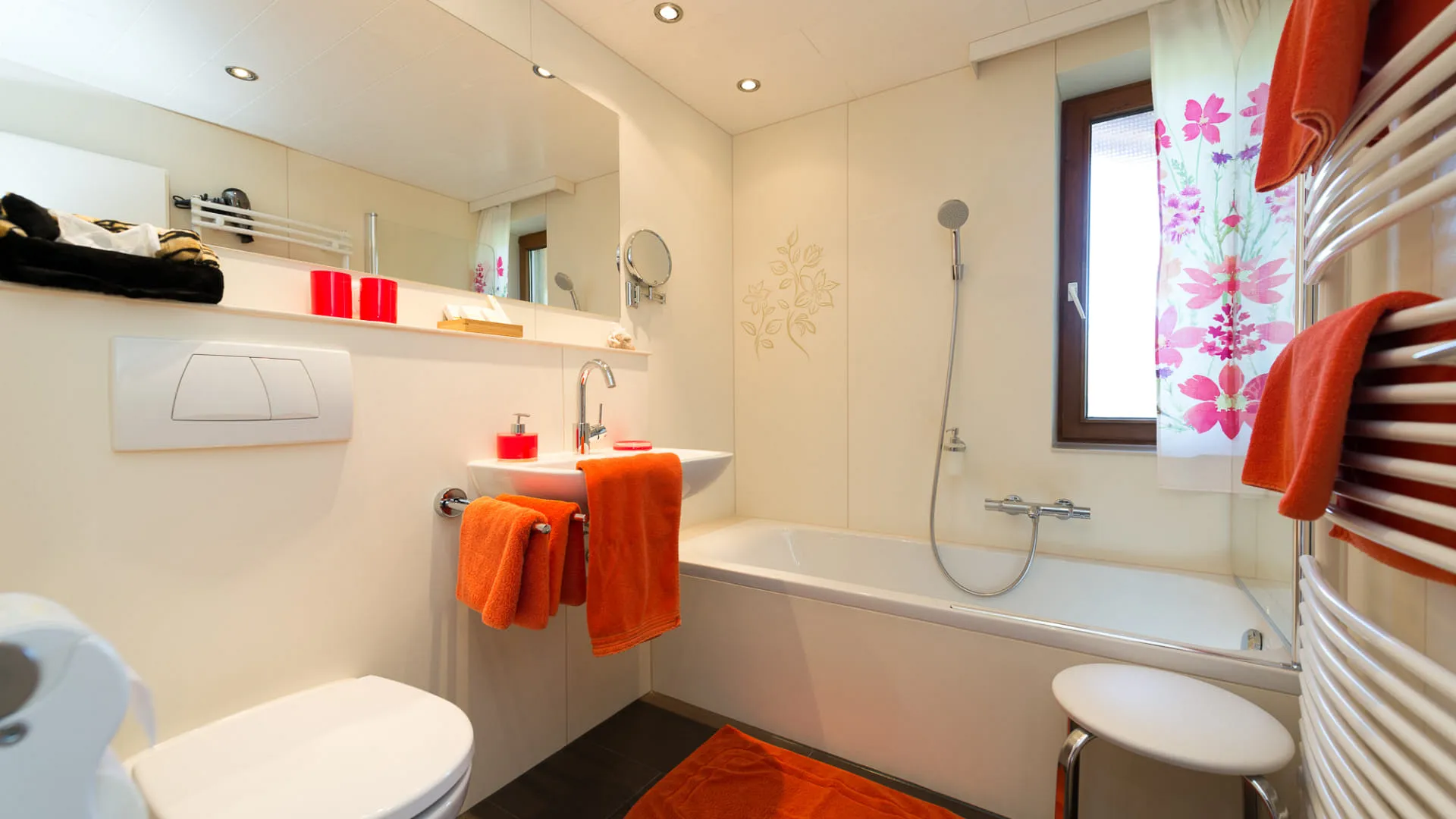 Helles Badezimmer mit Badewanne, Handtüchern und orangefarbener Dusche.