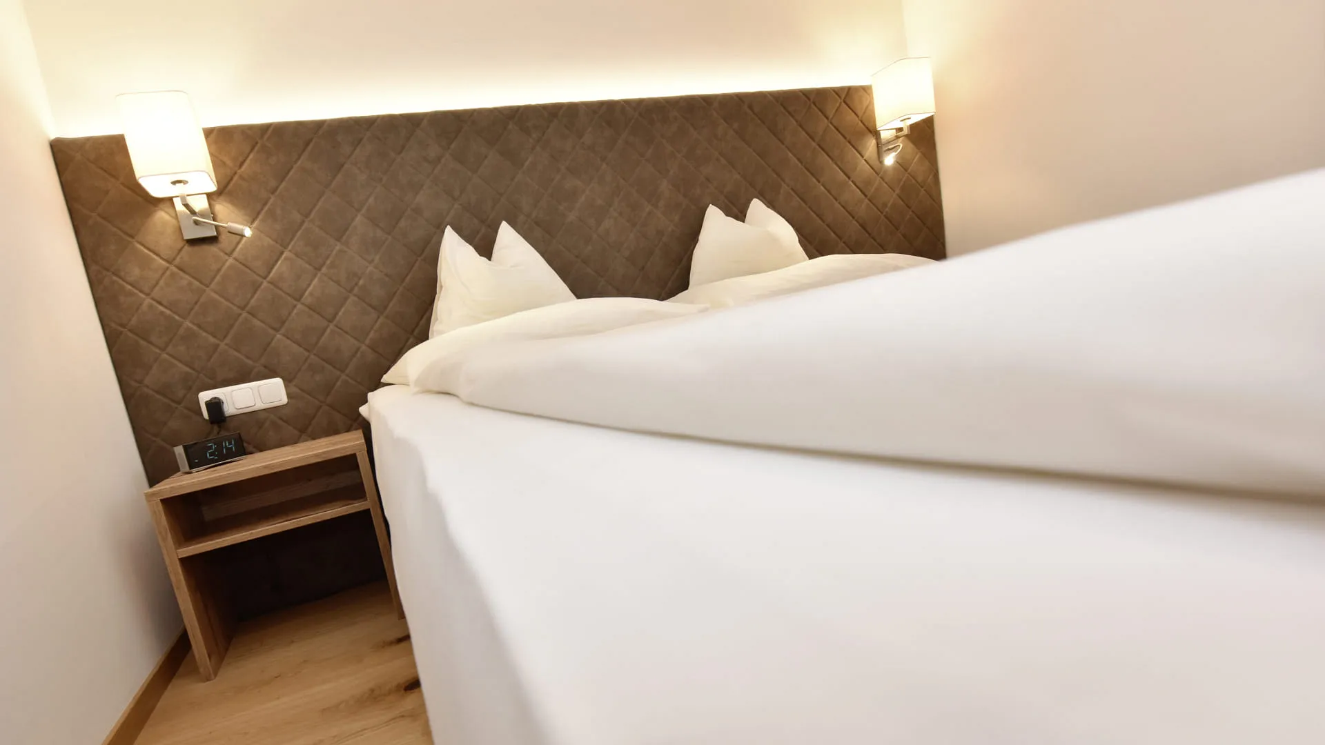 Ein Schlafzimmer mit einem Bett und zwei Kopfkissen, Nachttisch und Beleuchtung.