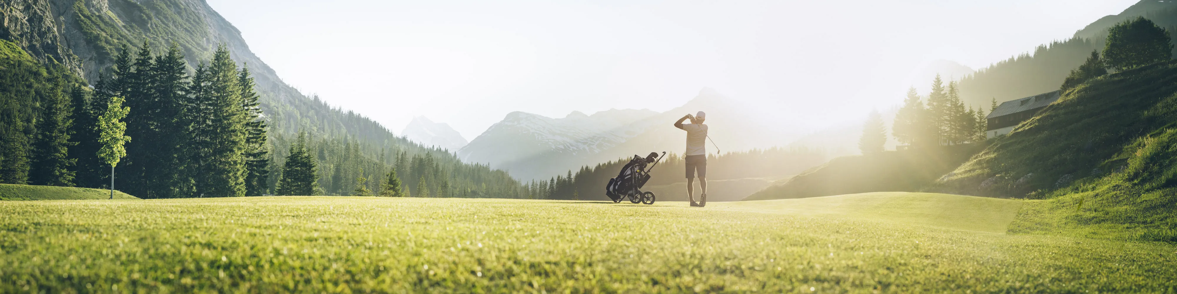 Golfplatz mit Spieler im Vordergrund, Berge im Hintergrund