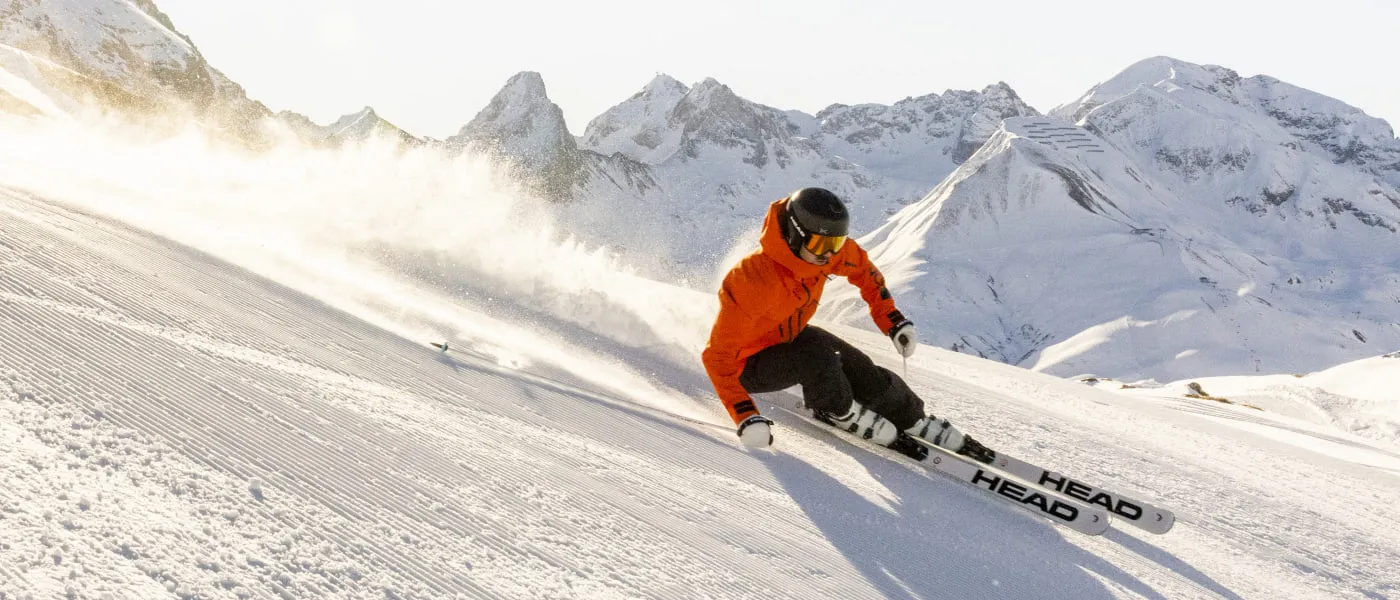 Skifahrer in orange auf verschneiter Piste mit Bergen im Hintergrund