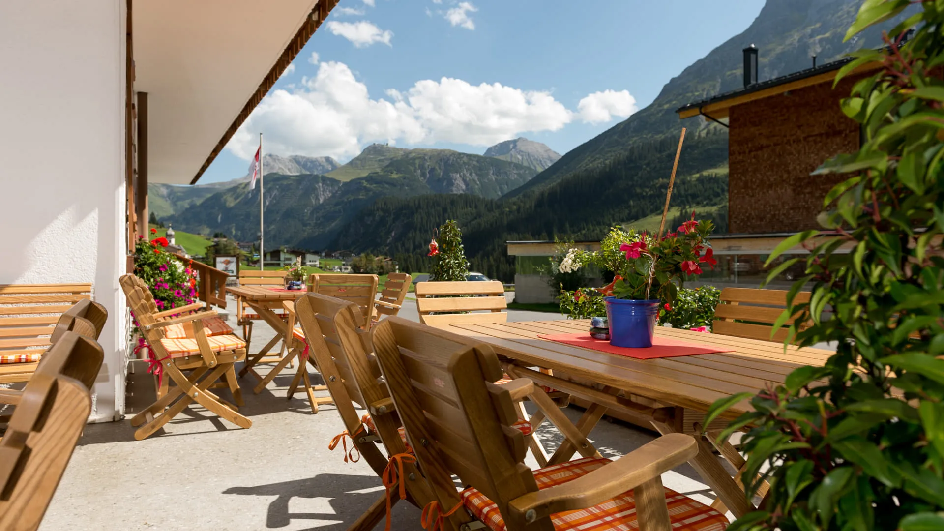 Blick auf eine Berglandschaft von einer Terrasse mit Holztischen und Stühlen